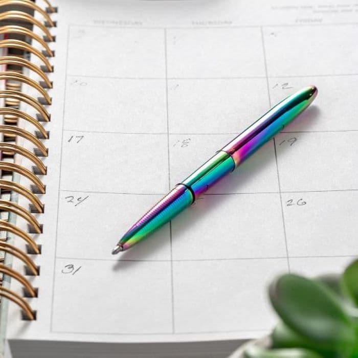 Open 400RB rainbow titanium nitride bullet space pen laying atop a spiral bound calendar